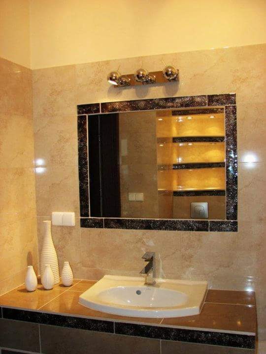 Wykończona łazienka z beżowymi płytkami, lustrem w czarnej ramie i białymi wazonami dekoracyjnymi na blacie