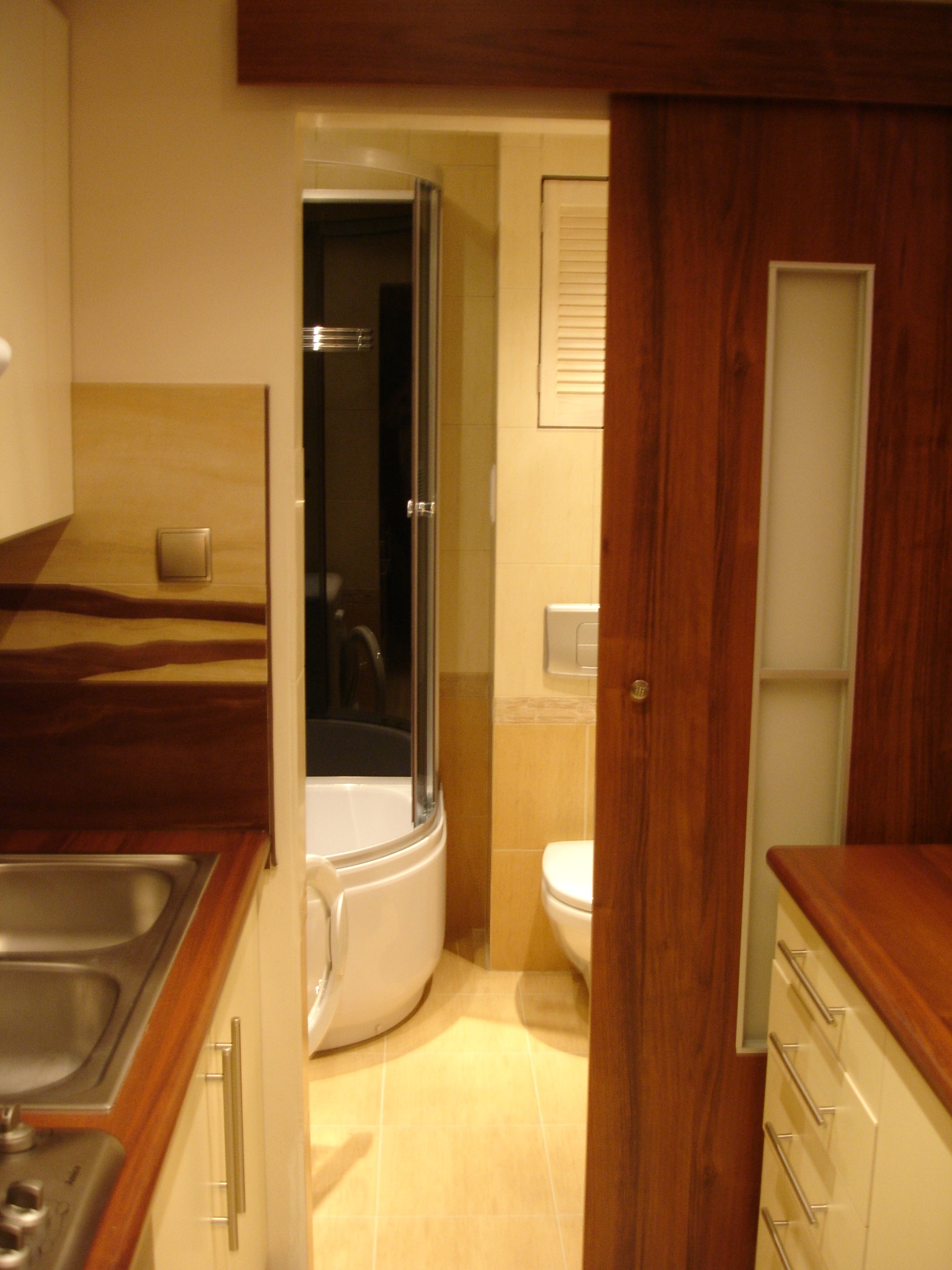 Nowoczesna łazienka z kabiną prysznicową narożną i przesuwnymi drzwiami z drewna, widok z kuchni.