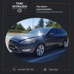 Szary samoch&oacute;d typu kombi na parkingu, z widocznym logo i napisem 'Wynajem samochod&oacute;w kr&oacute;tko/długoterminowy', oferta z Tarnowa.