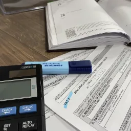 Formularz VAT-7, kalkulator, otwarty kalendarz i zakreślacz na biurku, przygotowane do rozliczeń podatkowych.