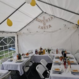 Strefa Polskiego Smaku - Uroczystość Pierwszej Komunii Świętej Jasia w białym namiocie, stoły z białymi obrusami, białe krzesła, balony białe i żółte, dekoracja z napisem 'I Komunia Św. Jasia'.