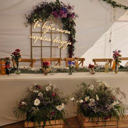 Strefa Polskiego Smaku - Uroczysty stół w namiocie: kwiaty, świece, napoje i dekoracja świetlna z napisem 'To była nasza wspólna decyzja'. Aranżacja eventowa z bliska.
