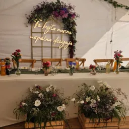 Uroczysty stół w namiocie: kwiaty, świece, napoje i dekoracja świetlna z napisem 'To była nasza wspólna decyzja'. Aranżacja eventowa z bliska.
