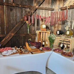 Strefa Polskiego Smaku - Rustykalny stół cateringowy z wędlinami, serami i dekoracjami na tle drewnianej ściany w stodole. Ustawione jedzenie, kwiaty i dekoracje.