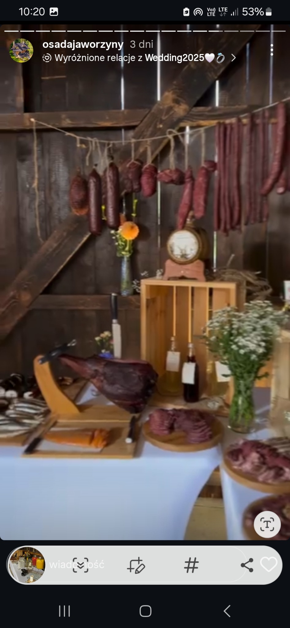 Rustykalny stół z wędlinami, szynką na stojaku, kwiatami w wazonie i dekoracjami na tle drewnianej ściany. Ujęcie z imprezy w stylu wiejskim.