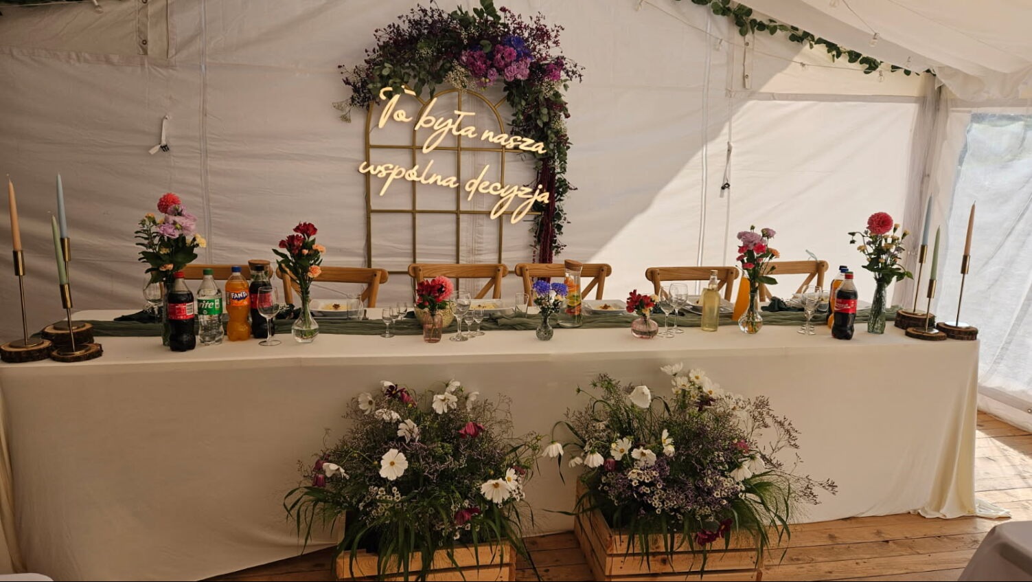 Uroczysty stół w namiocie: kwiaty, świece, napoje i dekoracja świetlna z napisem 'To była nasza wspólna decyzja'. Aranżacja eventowa z bliska.