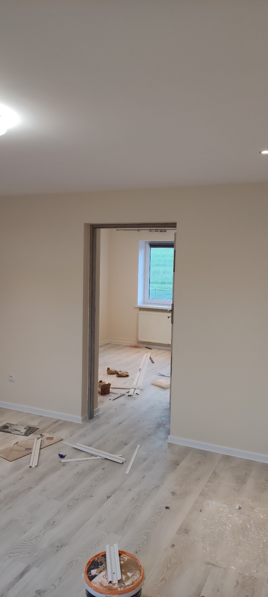 Jasne panele podłogowe w trakcie układania, widoczne listwy przypodłogowe, puszka z klejem i częściowo zamontowane ościeżnice drzwi.
