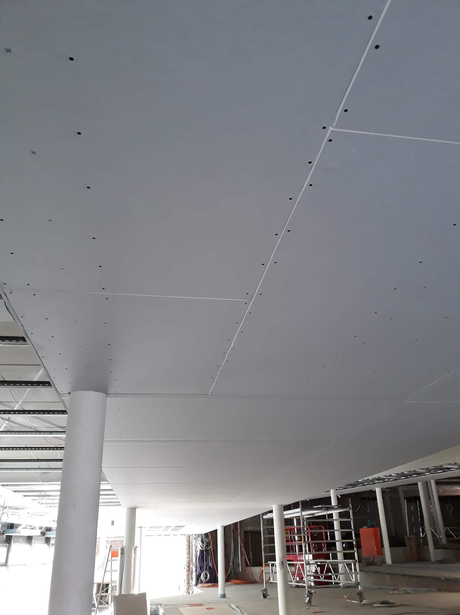 Sufit z płyt gipsowo-kartonowych, widoczne łączenia i wkręty, w tle kolumny i rusztowanie.