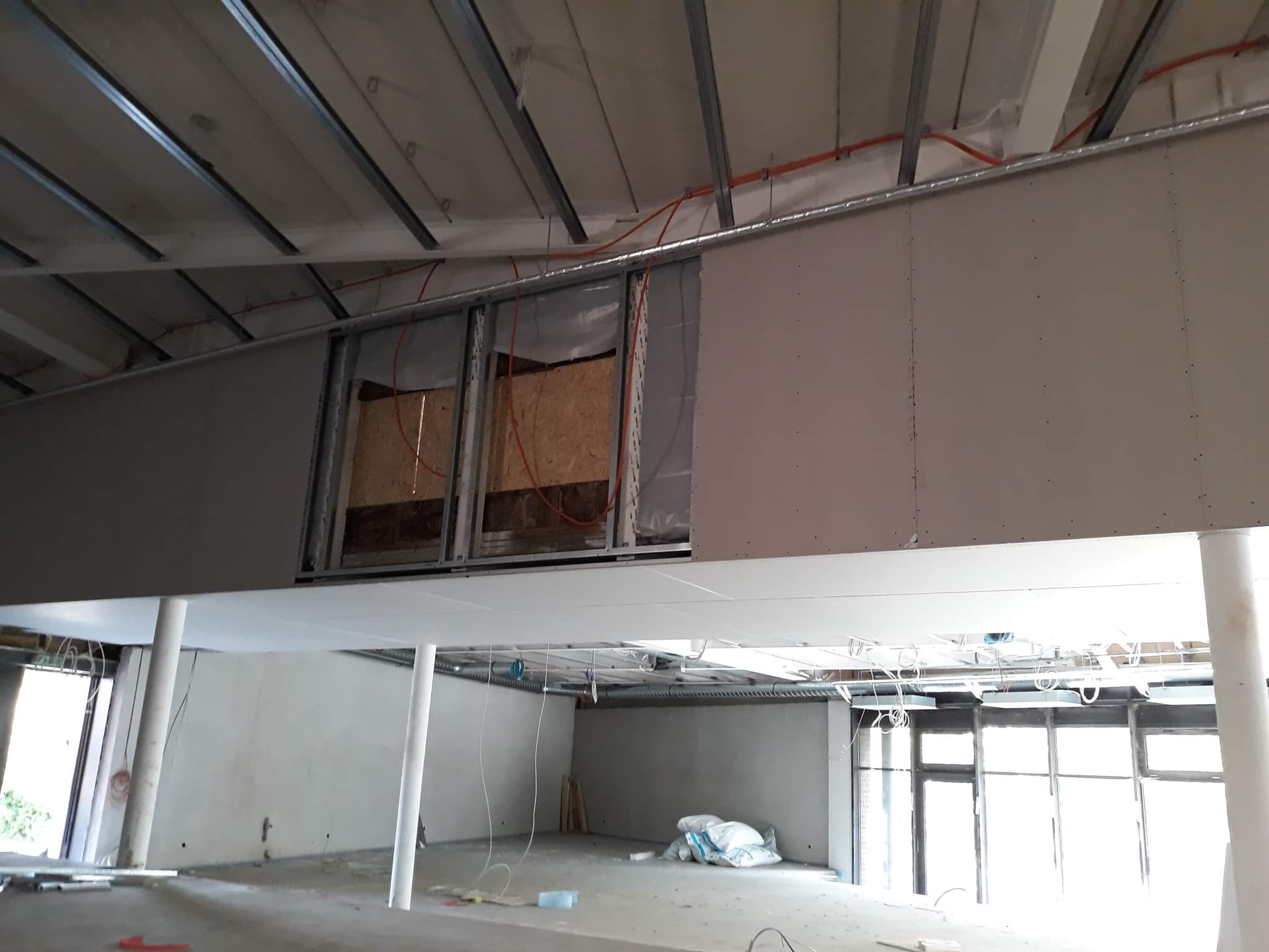 Montaż sufitu podwieszanego z płyt karton-gips, widoczne metalowe profile, instalacje elektryczne i częściowo zabudowane otwory w suficie.