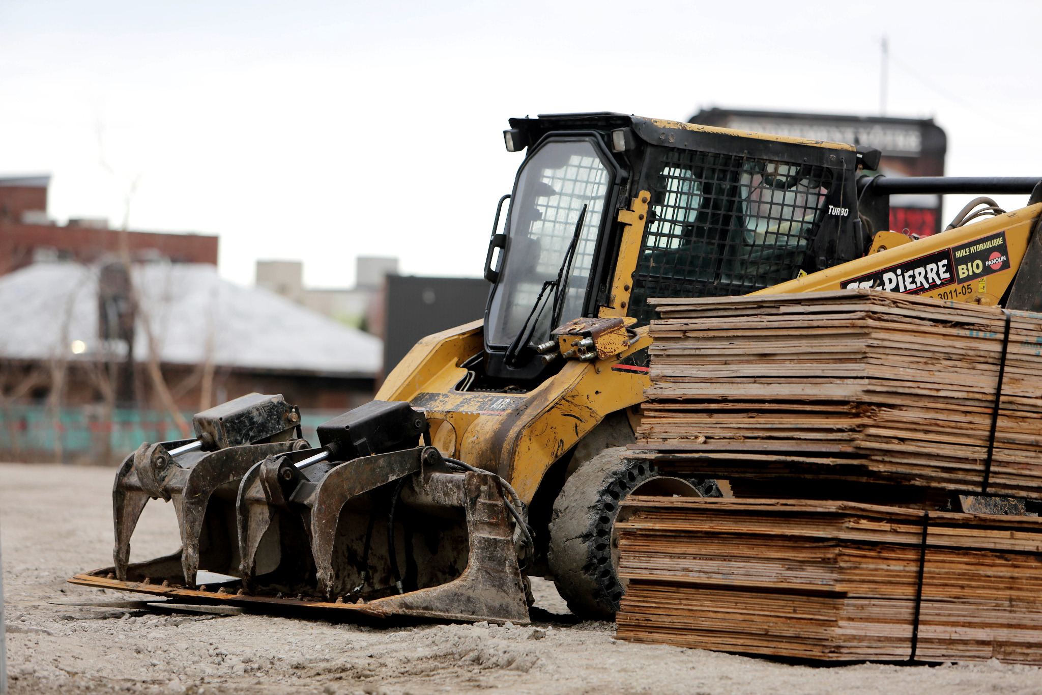 Żółta ładowarka teleskopowa z chwytakiem do drewna, zaparkowana w Zgierzu obok stosu płyt drewnianych na placu budowy.