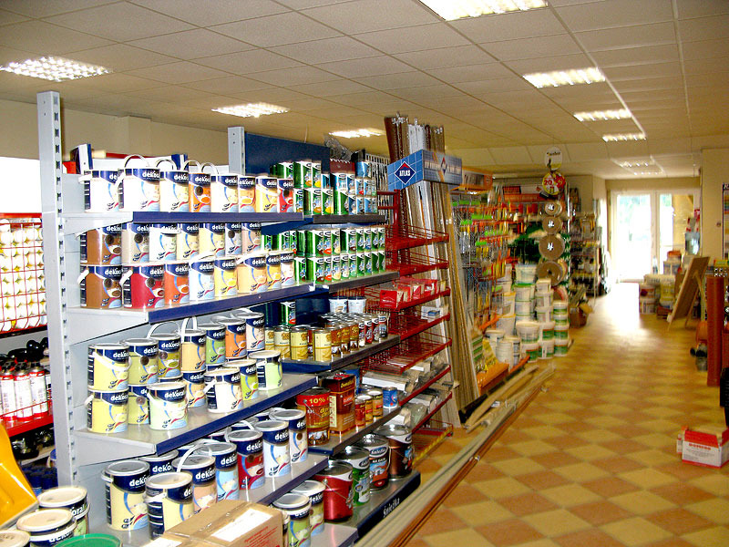 Wnętrze sklepu z materiałami budowlanymi, regały wypełnione puszkami farb, narzędziami i innymi artykułami budowlanymi, widok w głąb sklepu.