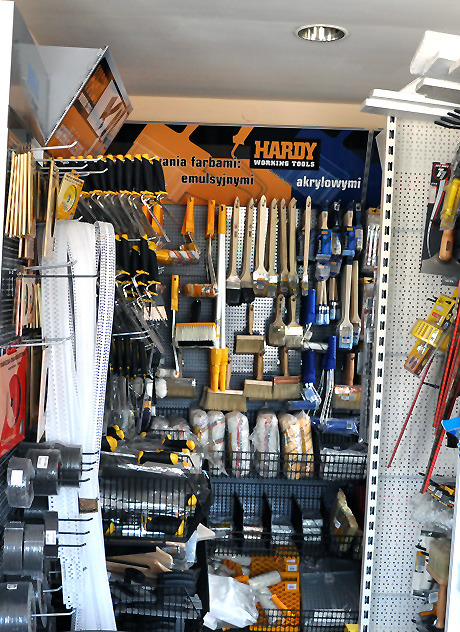 Ekspozycja różnorodnych pędzli malarskich, wałków i akcesoriów malarskich na metalowym regale w sklepie, z widocznym logo producenta Hardy i informacją o farbach emulsyjnych i akrylowych.