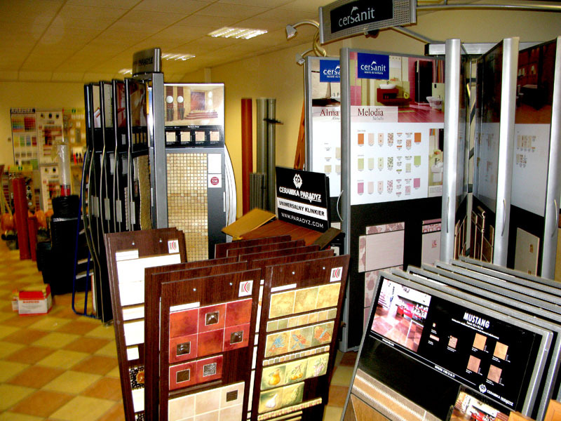 Ekspozycja płytek ceramicznych w sklepie budowlanym, prezentacja różnych wzorów i kolorów na stojakach i w panelach ekspozycyjnych, widoczne logo Cersanit i Ceramika Paradyż.