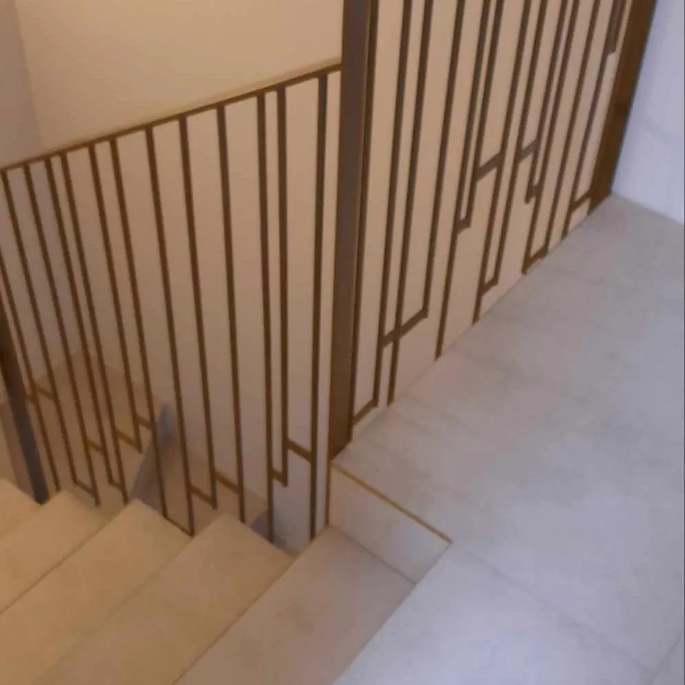 Nowoczesne schody z metalową balustradą o geometrycznym wzorze, widok z góry, jasne wnętrze.