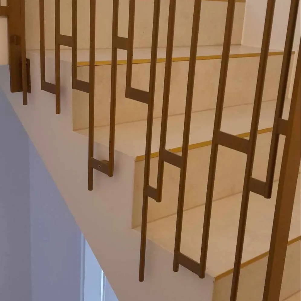Detal schodów z geometryczną balustradą w odcieniach złota, widok z dołu, jasne płytki na stopniach.