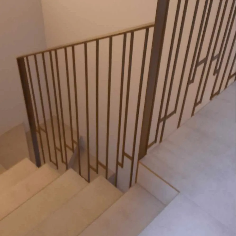Wewnętrzne schody z jasnymi stopniami i metalową balustradą o geometrycznym wzorze w odcieniach złota, widziane z góry.
