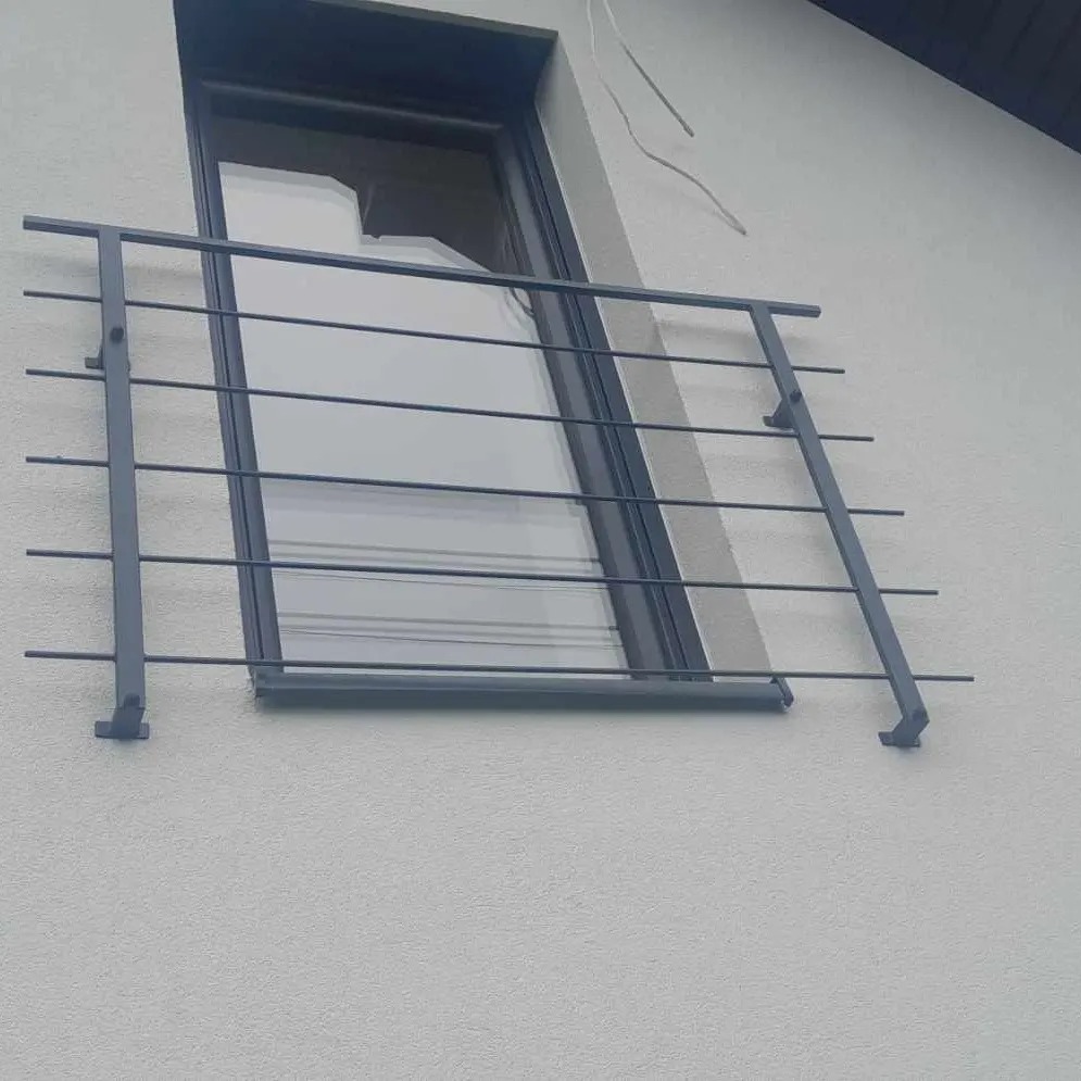 Metalowa balustrada okienna w kolorze grafitowym, zamontowana na elewacji budynku o jasnej strukturze, widoczna z dołu pod kątem.