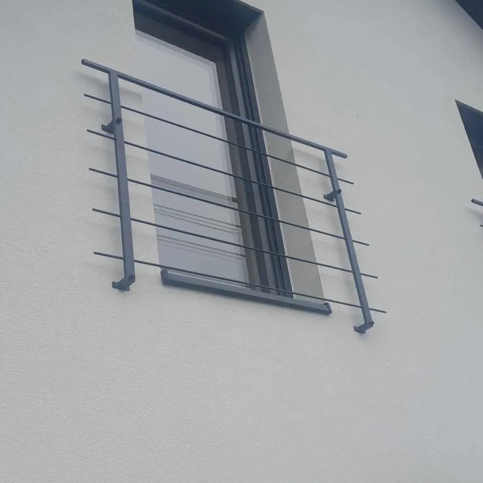 Metalowa barierka okienna z poziomymi prętami, zamontowana na elewacji budynku o jasnej strukturze, widoczna z dołu pod kątem.