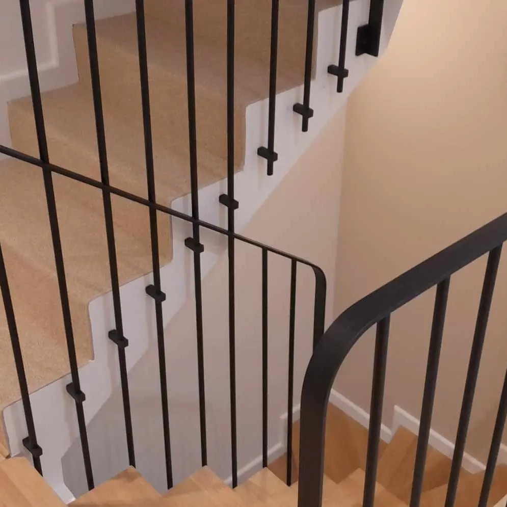 Klatka schodowa z drewnianymi stopniami pokrytymi wykładziną i czarną, metalową balustradą o minimalistycznym designie.