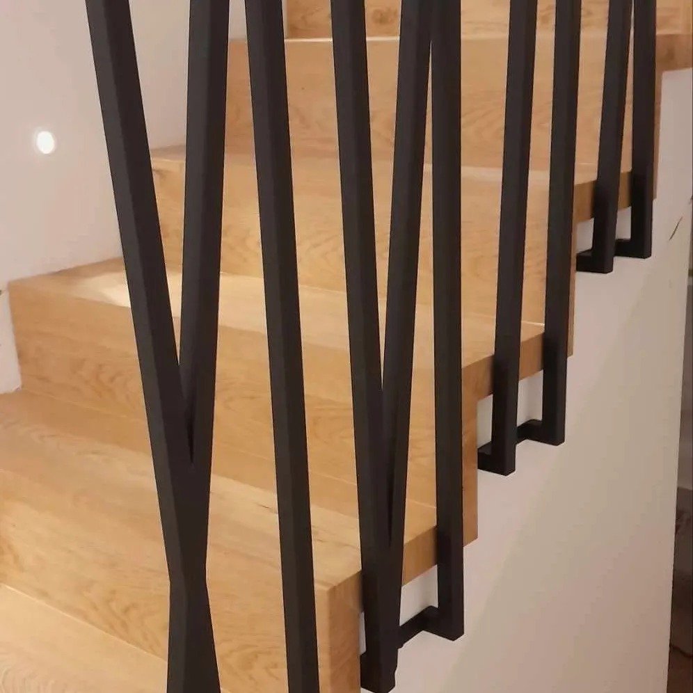 Nowoczesne schody z drewnianymi stopniami i czarną, metalową balustradą o nietypowym, geometrycznym wzorze.