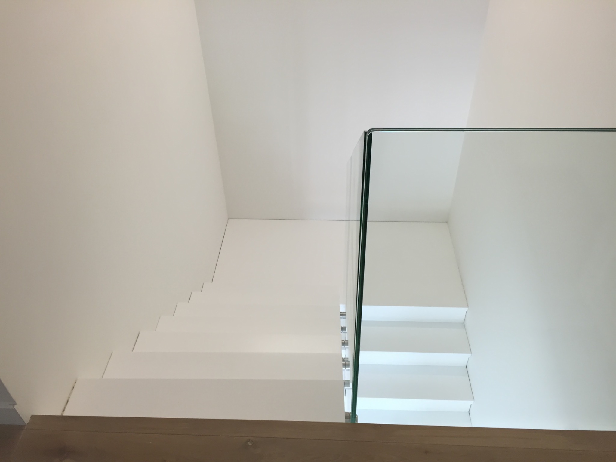 Nowoczesne, minimalistyczne schody z białymi stopniami i szklaną balustradą, widok z dołu na górę.