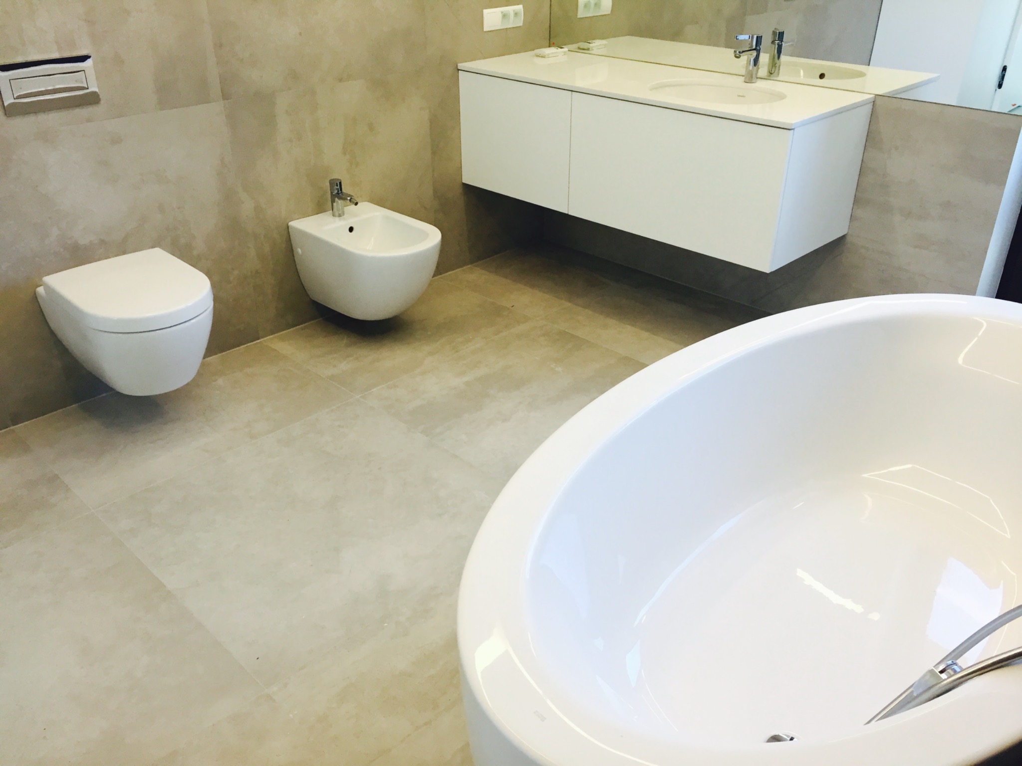 Nowoczesna łazienka z wanną, bidetem i podwieszaną toaletą, wykończona płytkami w odcieniach beżu.