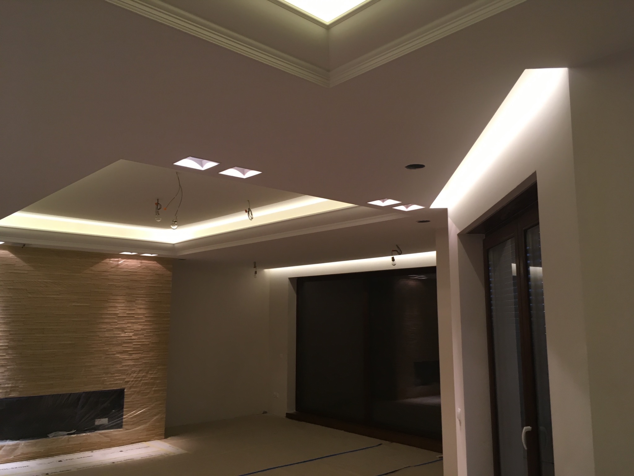 Oświetlenie LED w podwieszanym suficie z listwami i punktowymi lampami, ściana wykończona kamieniem dekoracyjnym, podłoga zabezpieczona folią malarską.