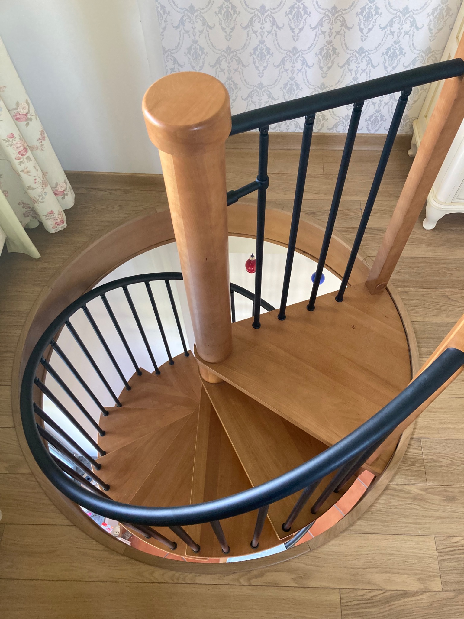 Widok z góry na drewniane schody spiralne z czarną, metalową balustradą, widoczne dekoracje świąteczne w tle oraz parkiet na podłodze.