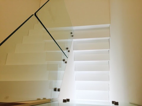 Nowoczesne, minimalistyczne schody z białymi stopniami i szklaną balustradą mocowaną punktowo, widok z dołu.