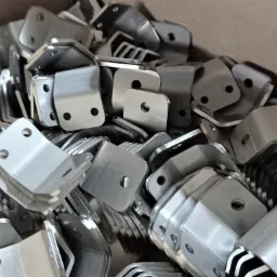 Stalowe, kątowe wsporniki z otworami ułożone w stosie, widoczne ślady obróbki.