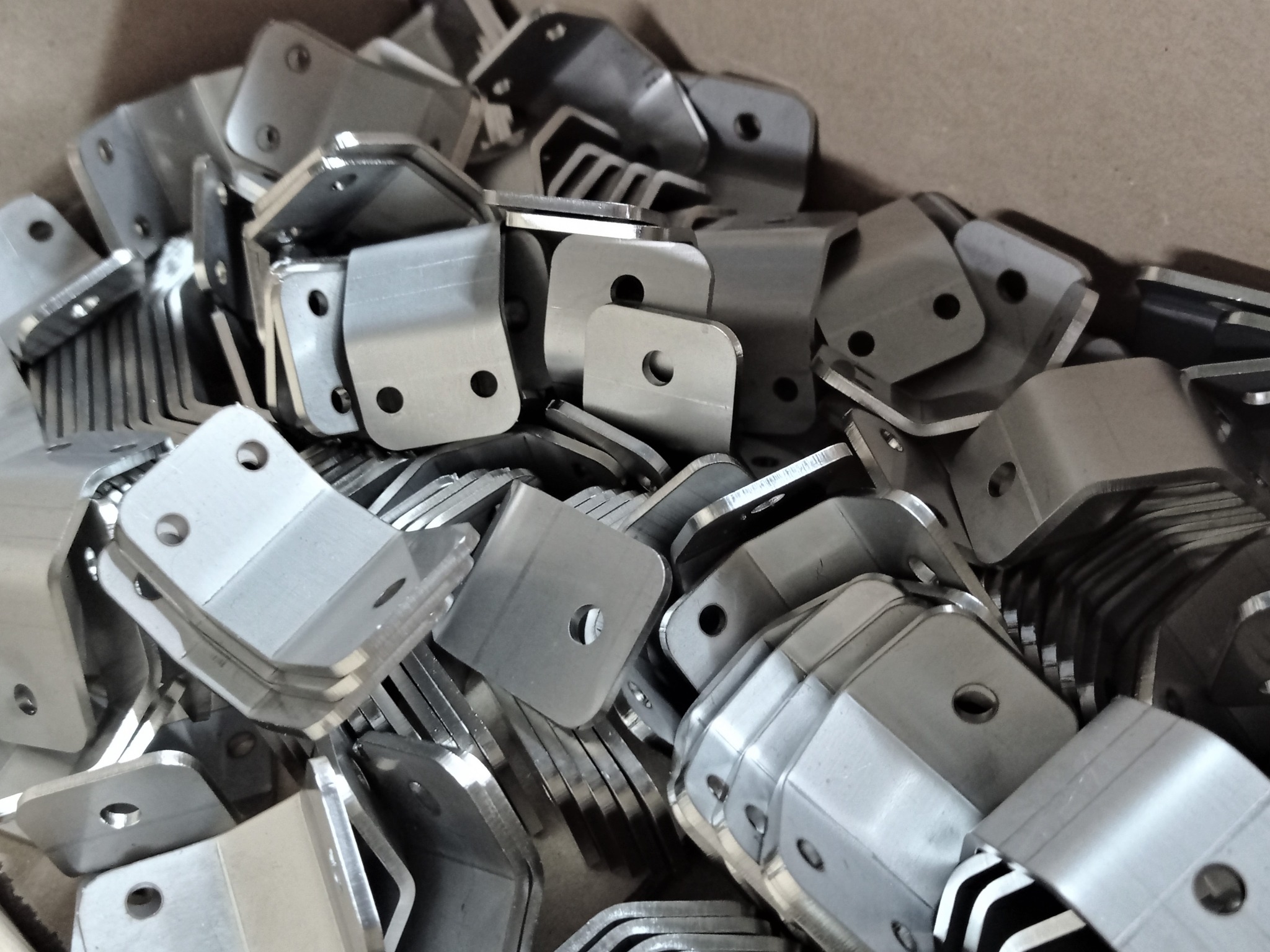 Stalowe, kątowe wsporniki z otworami ułożone w stosie, widoczne ślady obróbki.