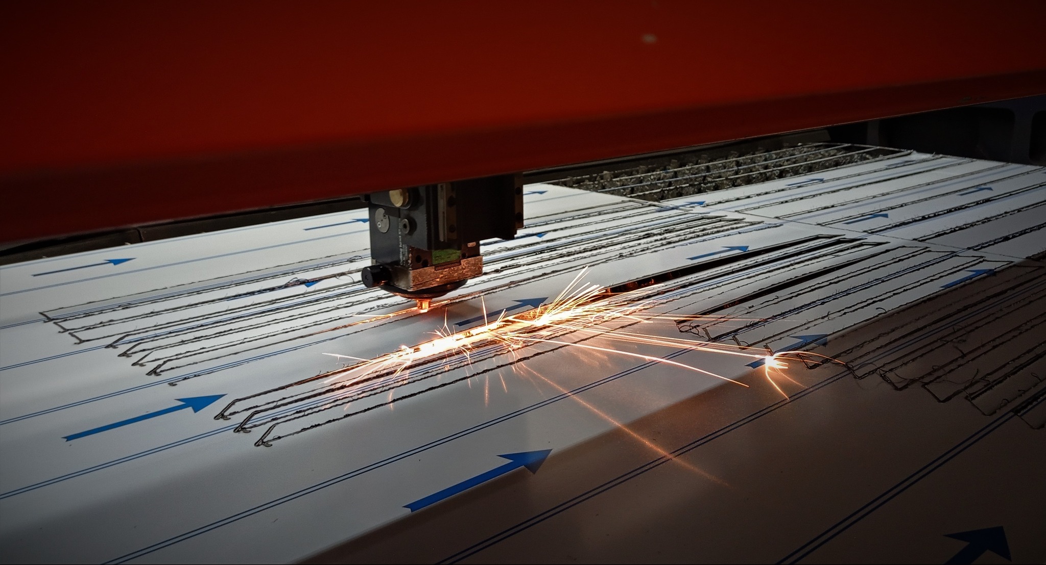 Precyzyjne cięcie metalu laserem z iskrami, widoczne ślady cięcia wzdłuż niebieskich linii.