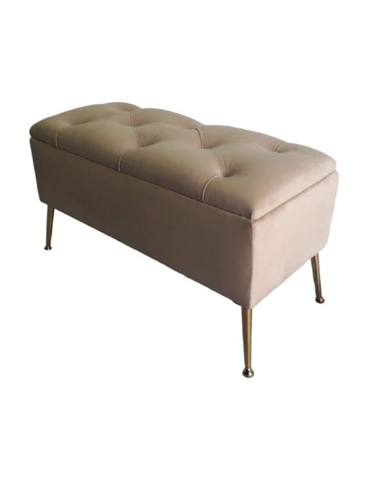 Beżowa, tapicerowana pufa ze schowkiem, z pikowanym siedziskiem i złotymi nóżkami, ustawiona na białym tle.