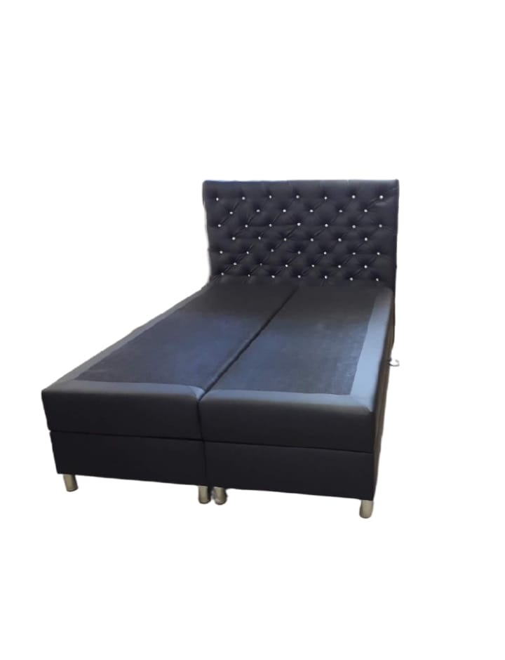 Czarne, tapicerowane łóżko kontynentalne z wezgłowiem pikowanym kryształkami, na srebrnych nóżkach.