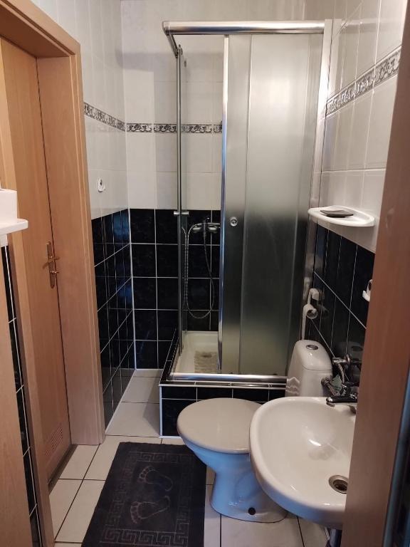 Wnętrze łazienki z kabiną prysznicową z przesuwnymi drzwiami, toaletą, umywalką i dywanikiem z odciśniętymi stopami.