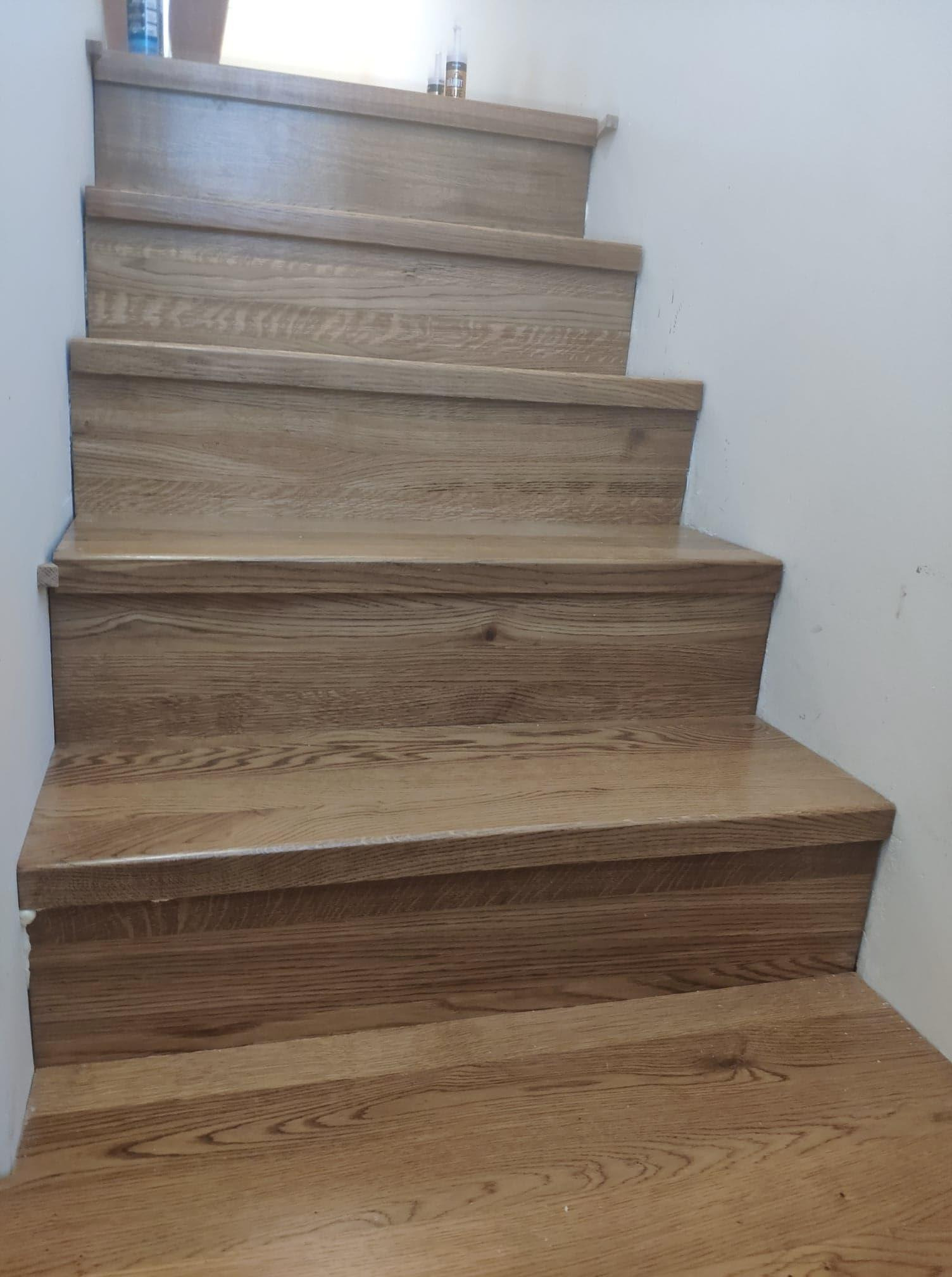 Wykończone drewniane stopnie schodowe z widocznym uszczelniaczem silikonowym przy ścianie.