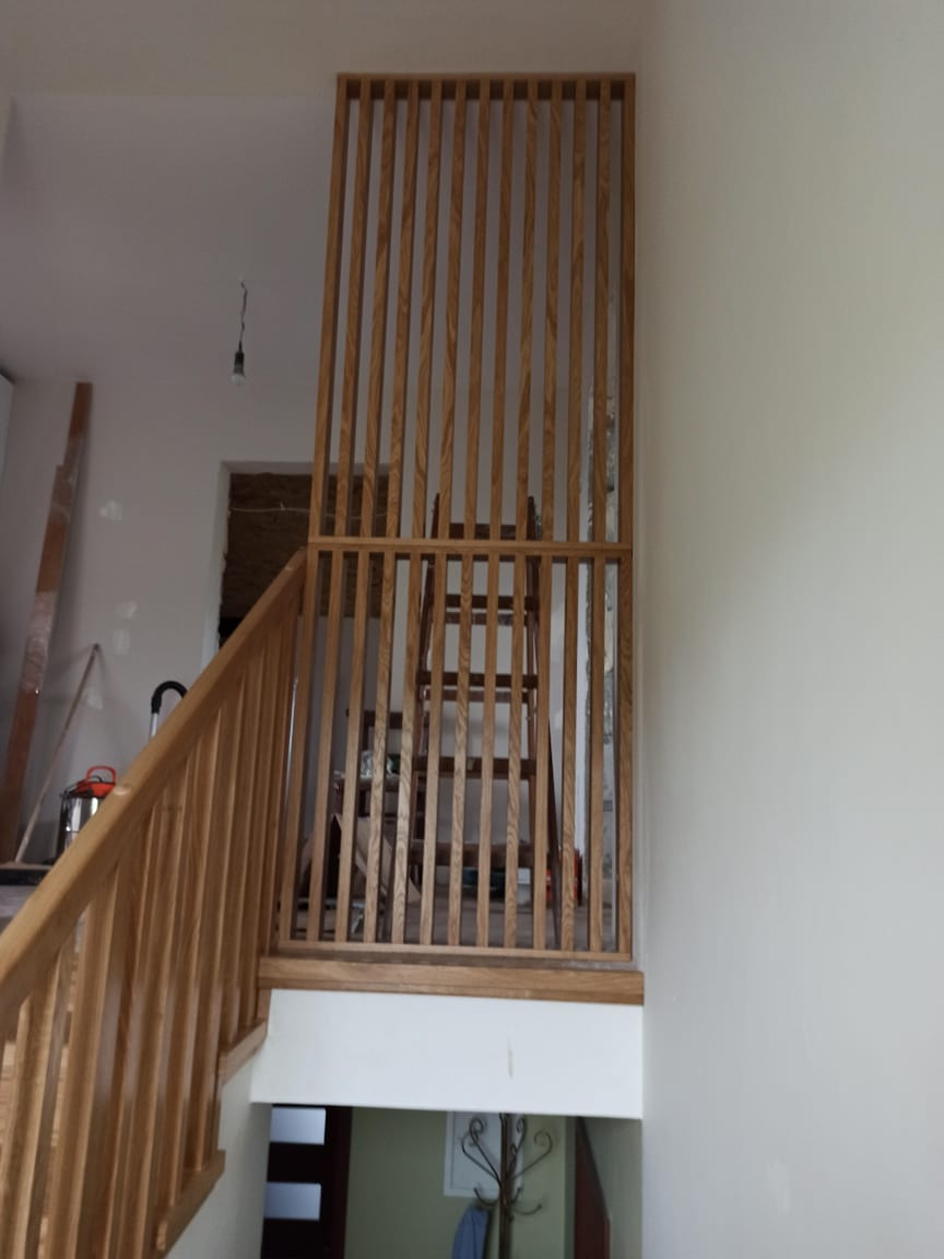 Drewniana balustrada z pionowych listew oddzielająca schody od antresoli, widoczna drabina w tle, surowy stan wykończenia wnętrza.