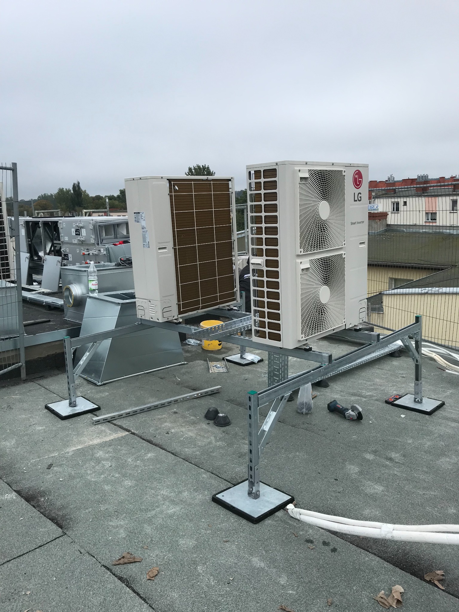 Dwie jednostki zewnętrzne klimatyzacji LG Smart Inverter zamontowane na metalowej konstrukcji na dachu budynku w Poznaniu, widoczne narzędzia i elementy instalacji.