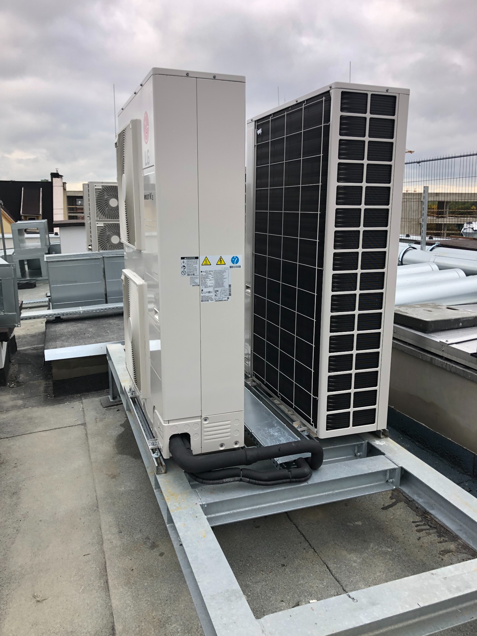 Zewnętrzne jednostki klimatyzacji LG Multi V S na dachu budynku, widoczne rury i stalowa konstrukcja wsporcza, w tle inne urządzenia i barierki.