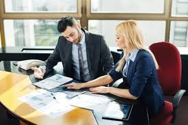 Mężczyzna i kobieta w biurze analizują dokumenty finansowe przy biurku, widoczne wykresy i tabele.