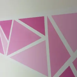 Ściana wewnętrzna pomalowana w geometryczne wzory z tr&oacute;jkąt&oacute;w w odcieniach r&oacute;żu i bieli, widoczny narożnik pokoju.