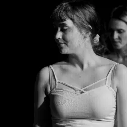 Portret kobiety w bieliźnie na czarnym tle, oświetlona bocznym światłem, z drugą osobą w tle.