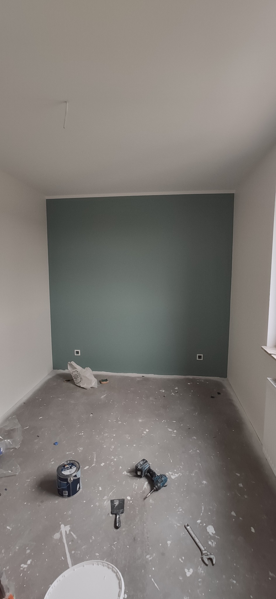 Pokój w trakcie malowania na kolor morski, widoczne narzędzia malarskie, puszki z farbą i ślady farby na podłodze.