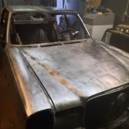 Karoseria samochodu przed malowaniem, po piaskowaniu w warsztacie w Poznaniu, widoczne ślady rdzy i przygotowania do dalszych prac blacharskich.