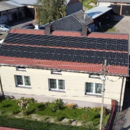 Dom jednorodzinny z panelami słonecznymi na dachu z czerwonej dachówki, widok z góry, słoneczny dzień.