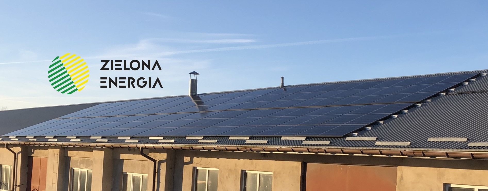 Instalacja paneli słonecznych na dachu budynku gospodarczego, widoczne logo firmy 'Zielona Energia' po lewej stronie.