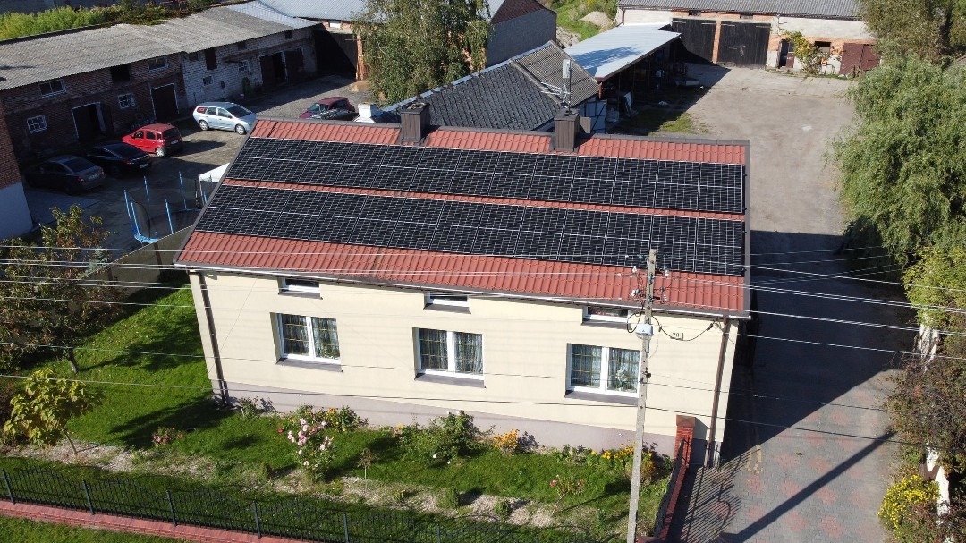 Dom jednorodzinny z panelami słonecznymi na dachu z czerwonej dachówki, widok z góry, słoneczny dzień.