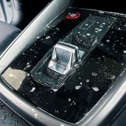KF Detailing Park - Błyszczący panel zmiany biegów w samochodzie, pokryty kroplami wody lub piany, sugerujący świeże czyszczenie wnętrza pojazdu. Widoczne przyciski i chromowane elementy.