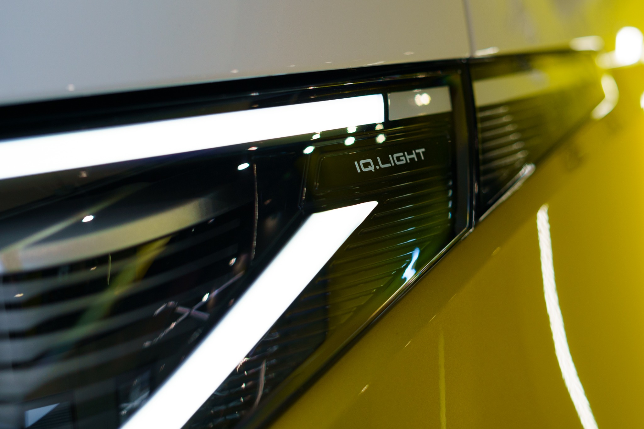 Żółty samochód z bliska, reflektor LED z napisem IQ.LIGHT, widoczne odbicie światła na karoserii.