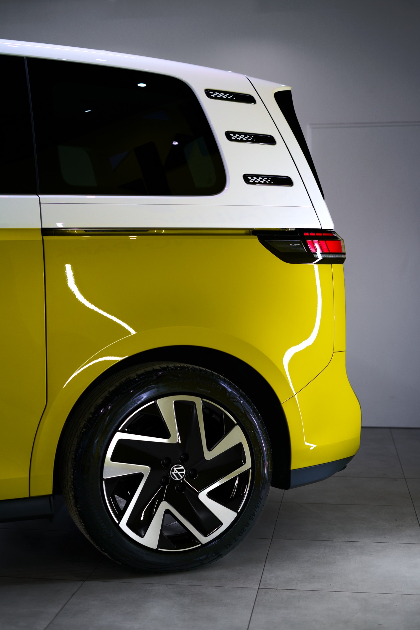Żółto-biały Volkswagen ID. Buzz z bliska, widoczny tylny błotnik, koło z aluminiową felgą i tylne światło, w studio detailingowym.